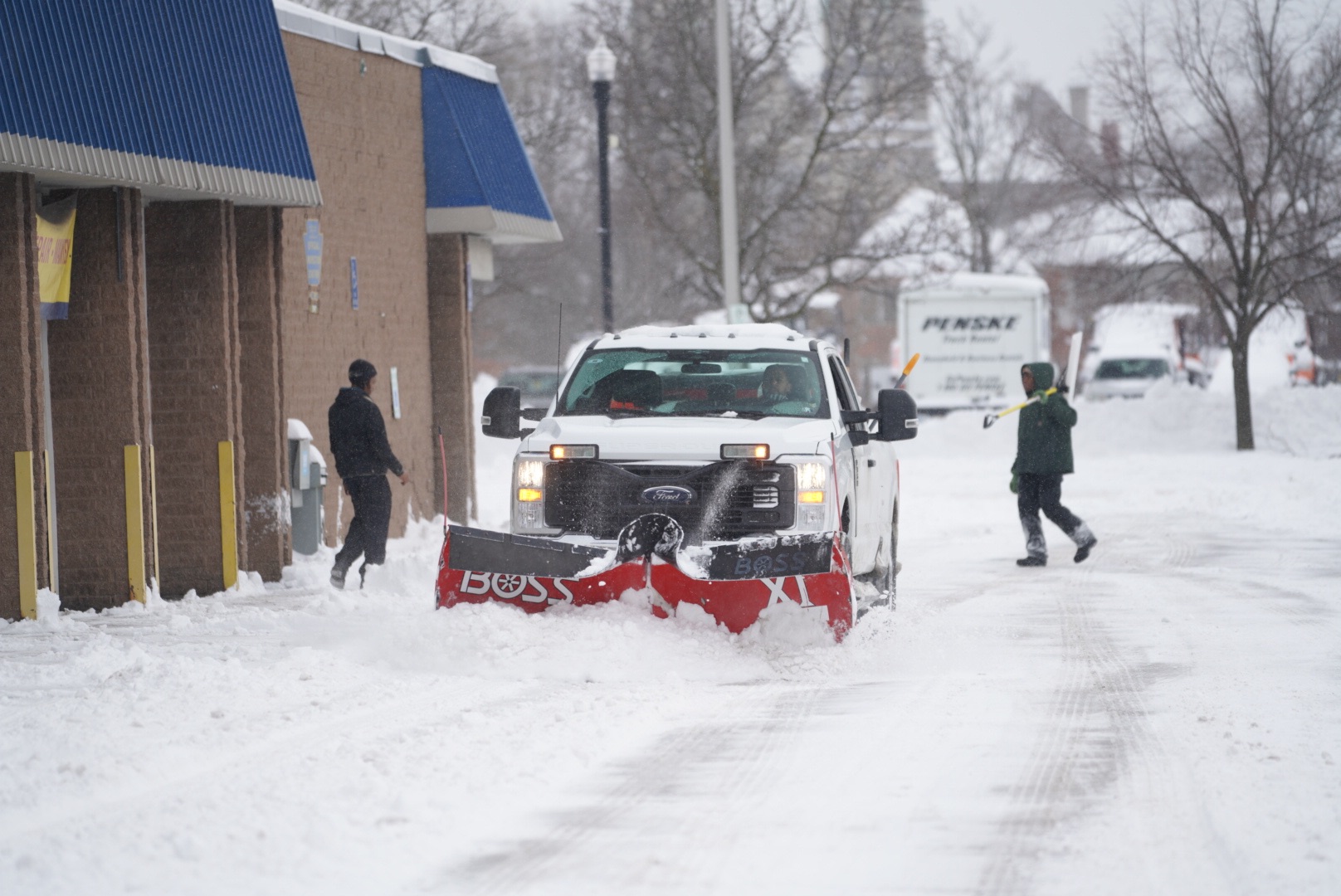 A Whitetail plow truck and crew clearing a commercial property during active snowfall.